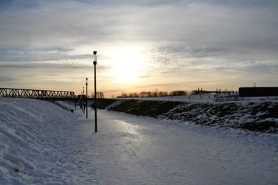 Snow covered street against sky during sunset