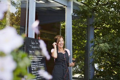 Happy cafe owner using headphones connected to mobile phone outside cafe