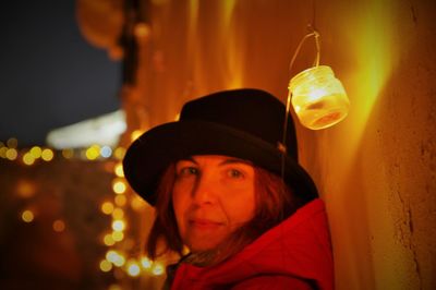 Portrait of woman wearing hat against illuminated light at night