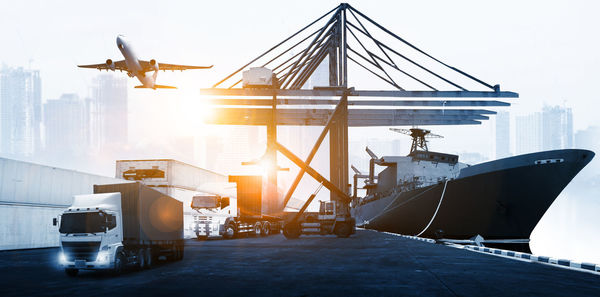 Cranes at harbor against sky during sunset