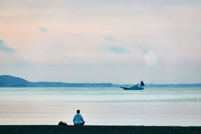 Rear view of men sitting on beach against sky