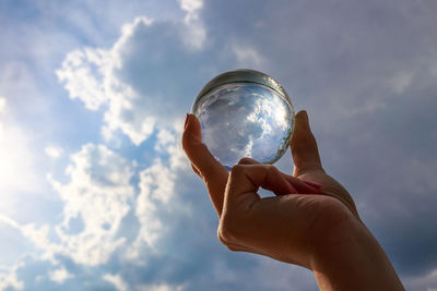 Cropped hand holding crystal ball against sky