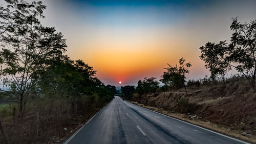 Road amidst trees against sky during sunset