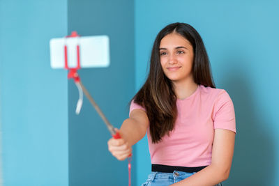 Portrait of a smiling young woman standing against blue wall