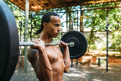 Shirtless young man holding barbell outdoors