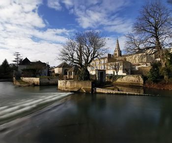 Buildings by river against sky