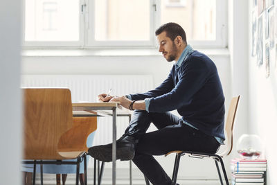 Side view of mid adult businessman writing in book at office desk