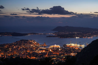 Aerial view of illuminated city by sea against sky