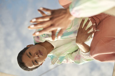 Portrait of woman with arms raised against sky