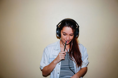 Young woman listening to music against wall