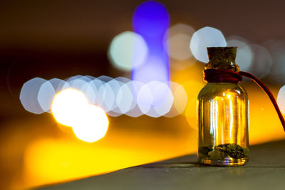 Close-up of glass bottle on table against colorful light