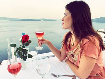 Midsection of woman with drink in sea against clear sky