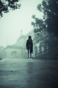 Full length of woman in mid-air over street against church during foggy weather