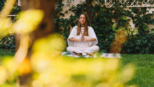 Full length of young woman meditating while sitting outdoors