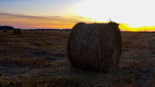 Hay bales on field against sky during sunset