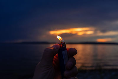 Midsection of man holding fire against sky at sunset