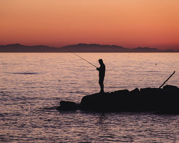 Silhouette man on boat on sea against orange sky during sunset