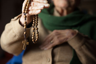 Midsection of senior woman holding wooden rosary beads with cross