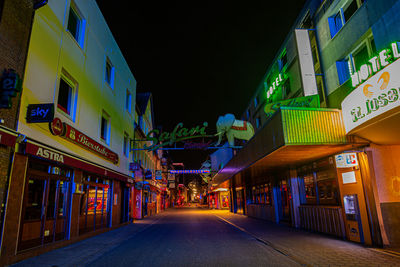 Illuminated street amidst buildings in city at night