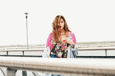 Woman standing by railing against clear sky