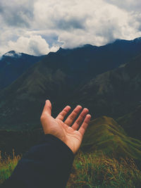 Cropped hand of person gesturing against mountains and sky