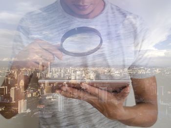 Reflection of man on glass window using digital tablet against cityscape