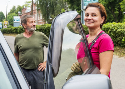 Portrait of smiling woman entering car on road in city