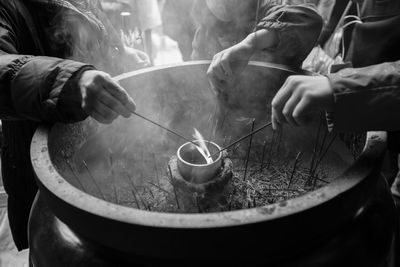 Midsection of people igniting incenses from fire