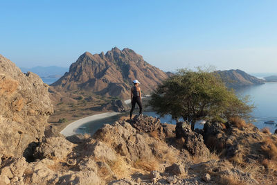 Rear view of woman standing on rock against sky