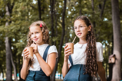 Two schoolgirls are drinking from eco-friendly cups and drinking straws in the park