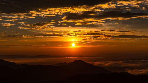 Scenic view of dramatic sky over silhouette landscape during sunset