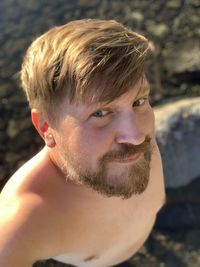 Portrait of shirtless bearded man on a rocky beach.