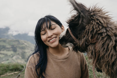 Smiling woman with eyes closed standing by alpaca