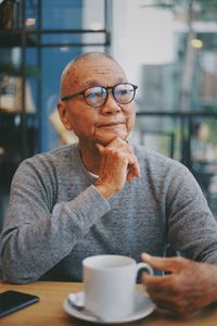 Thoughtful senior man with coffee on table sitting in cafe