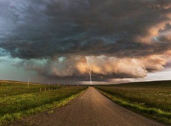 Country road amidst field against storm clouds