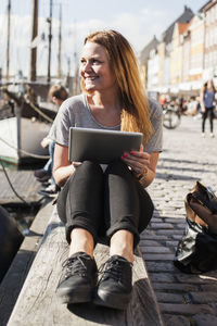 Happy woman with digital tablet sitting at harbor