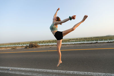 Full length of woman jumping on road against clear sky