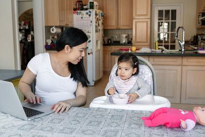 Asian chinese young mother with daughter baby working online from home on internet