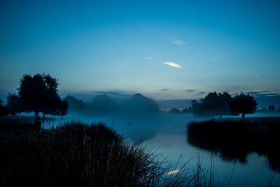 Silhouetted trees and lake against blue sky