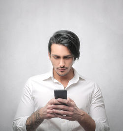 Young man using mobile phone against wall