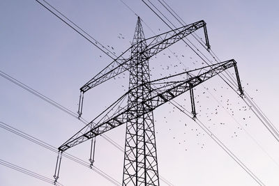 Low angle view of electricity pylon and flock of birds against clear sky