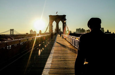 Rear view of man walking on brooklyn bridge during sunrise