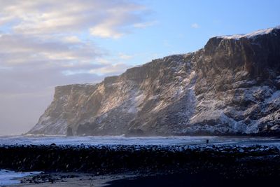 Scenic view of sea by mountain against sky