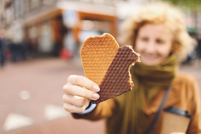 Young woman holding eaten heart shape waffle on walkway