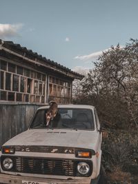 Woman sitting on car against sky