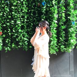 Woman holding camera while standing by plants