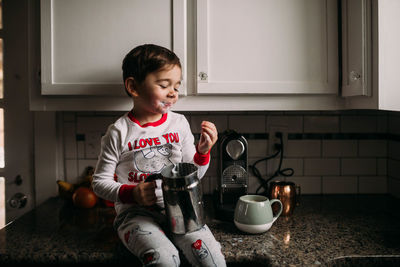 Preschool age boy sitting on kitchen counter with milk on face