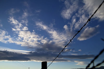 Low angle view of power lines against cloudy sky