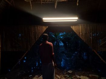 Rear view of woman standing against illuminated wall