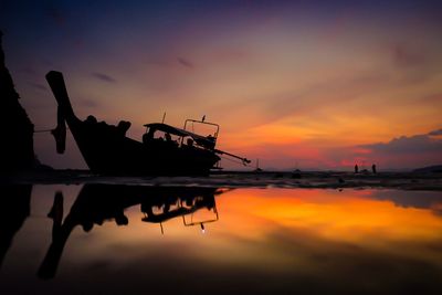 Silhouette man on boat moored in sea against sky during sunset